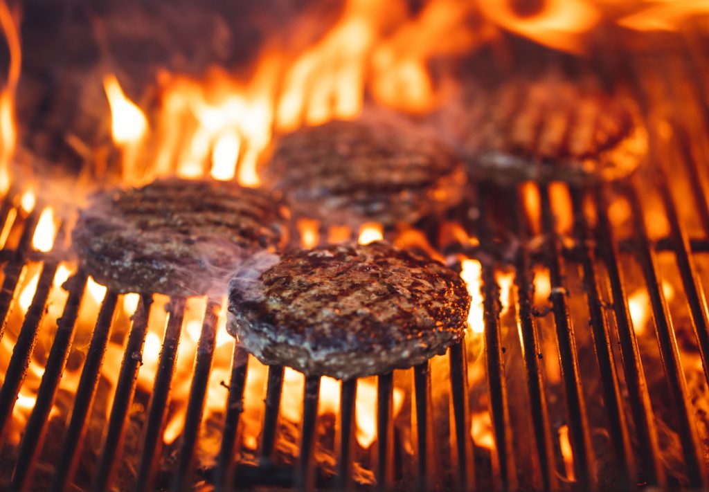 Picture shows three burger patties being cooked on top of a grill.